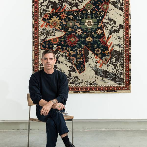 Jan Kath sitzt vor einem Teppichbild aus der Serie „Rug Bombs“.