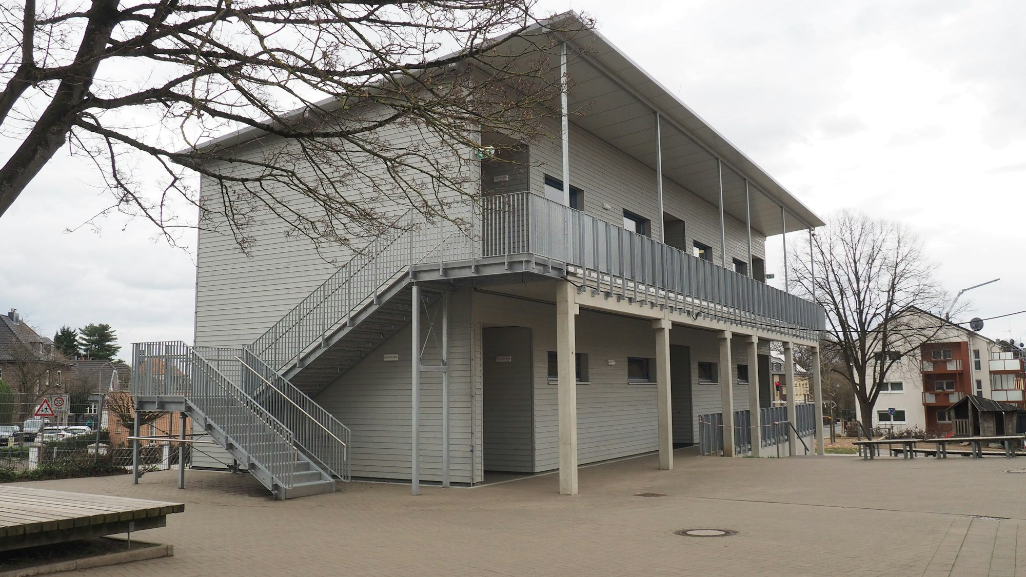 Das Foto zeigt ein graues zweigeschossiges Gebäude mit Außentreppe.
