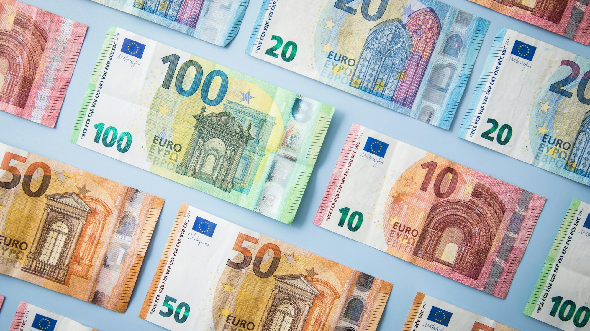 Geldscheine sind vor einem blauen Hintergrund nebeneinander aufgereiht.(Symbolbild)