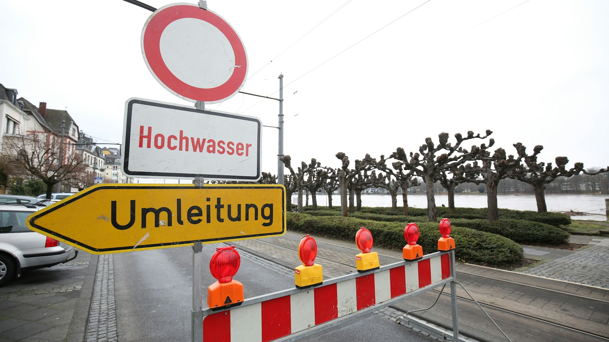 Ein Schild Hochwasser und eine Sperrbake stehen auf der Rheinallee in Königswinter. Auch eine Umleitung ist ausgeschildert.
