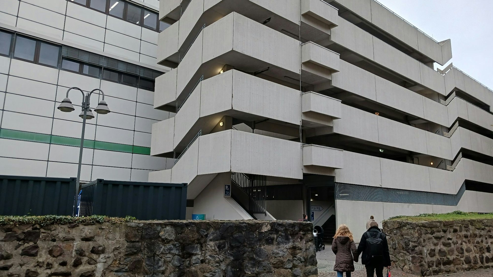 Eine alte Stadtmauer, dahinter ein großes Parkhaus aus Beton