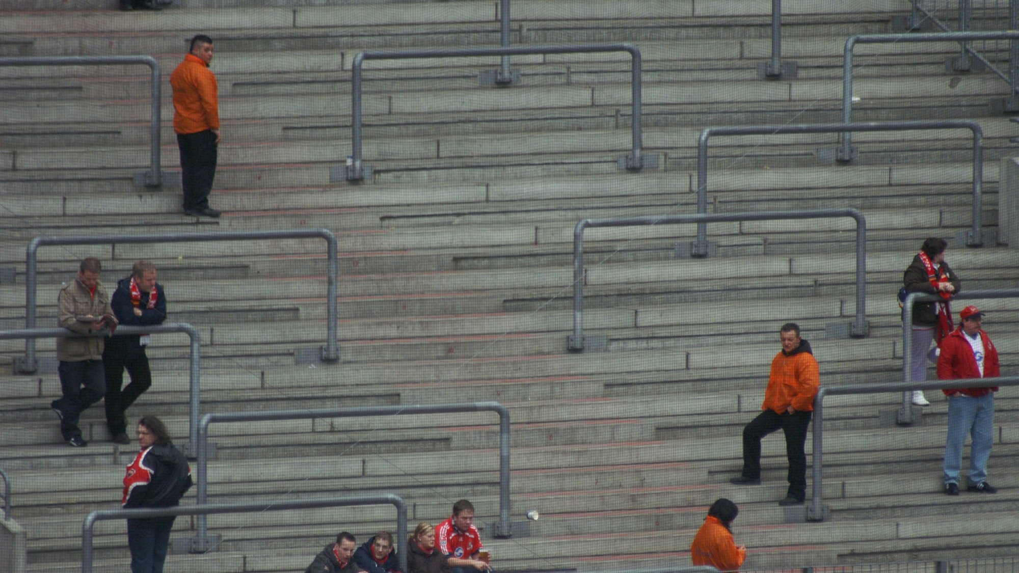 Wenige Fans und Ordner verlieren sich auf den Rängen eines Fußballstadions.