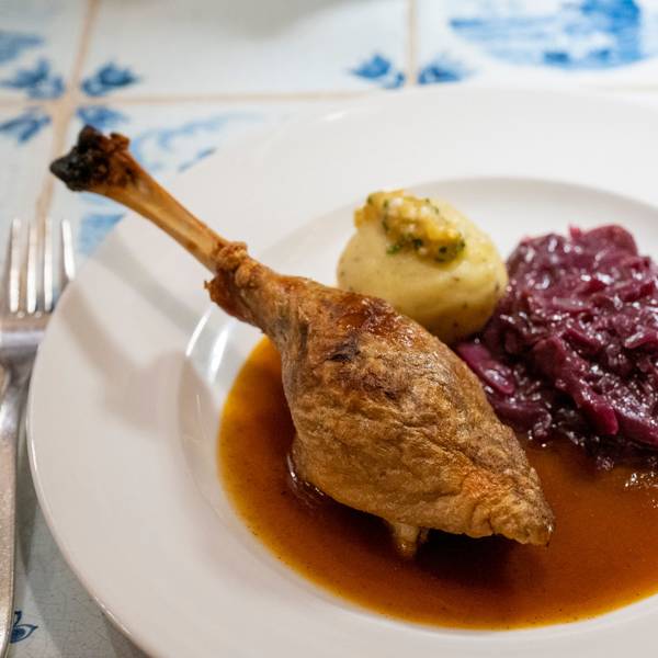 Ein gebratenes Stück Gans liegt mit Sauce, Rotkohl und Kloß auf einem Teller.