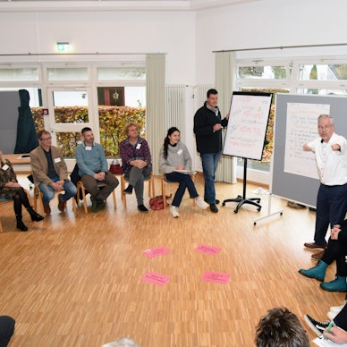 Unter der Moderation von Rainer Schmidt (rechts) ging es beim Auftaktworkshop in Wiehl-Oberbantenberg zunächst um das Verständnis von „Inklusion“. Hier steht der Moderator an einem Flipchart, die Teilnehmenden sitzen in einem Kreis um ihn herum.