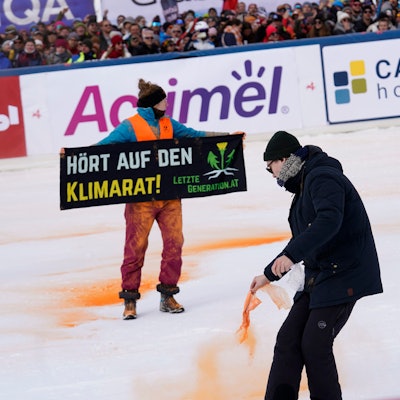 Ein Demonstrant der Letzten Generation versprüht Farbe im Zielbereich eines alpinen Skiweltcup-Slaloms der Herren in Gurgl.