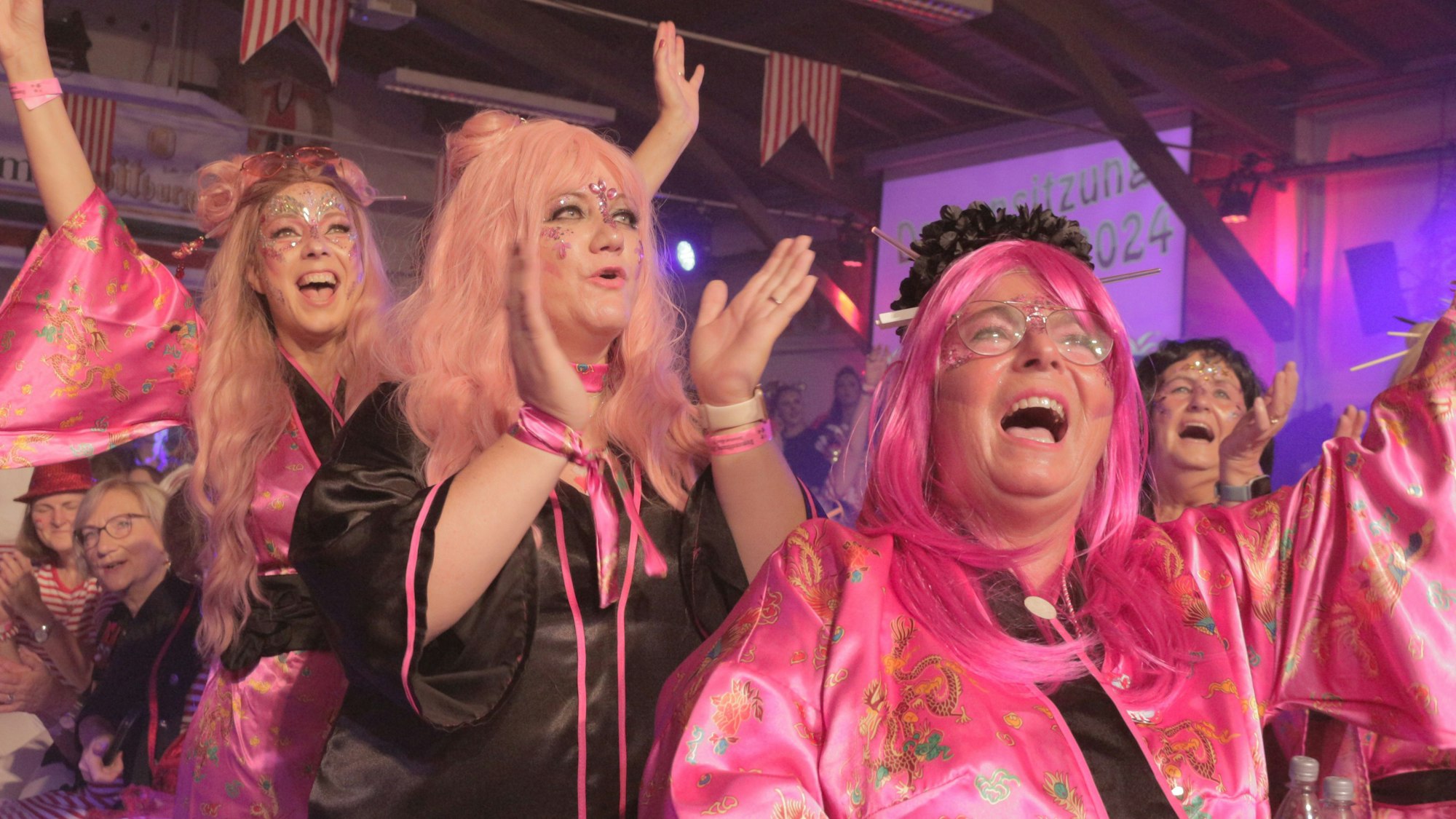 Geschminkte und kostümierte Frauen strecken gut gelaunt die Arme zum Alaaf-Ruf in die Höhe, einige von ihnen im Stehen.