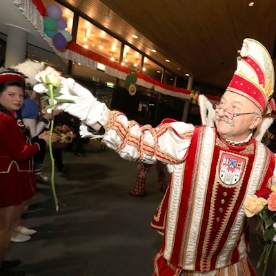 Eine Man im rot-weißen Prinzen-Ornat verteilt Rosen.