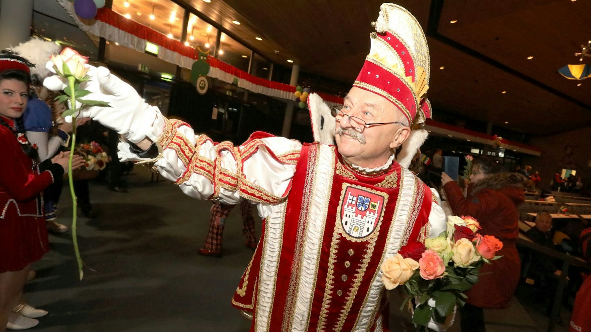 Eine Man im rot-weißen Prinzen-Ornat verteilt Rosen.