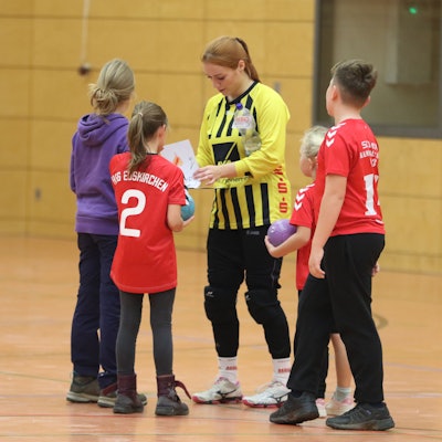 Das Bild zeigt Anna Kurm, die von jungen Fans umringt wird und Autogramme schreibt.