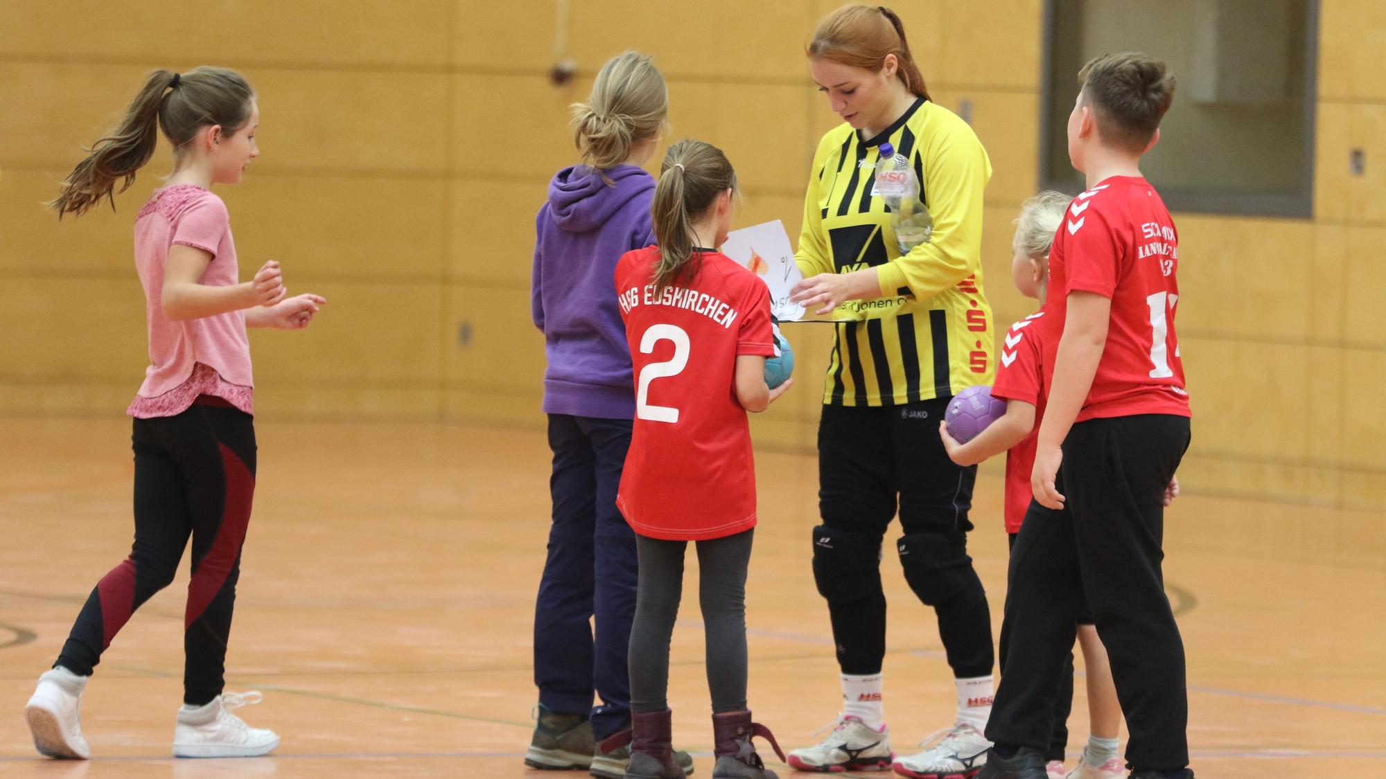 Das Bild zeigt Anna Kurm, die von jungen Fans umringt wird und Autogramme schreibt.