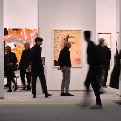 Die Silhouetten von Messebesuchern sind vor einem Messestand zu sehen.