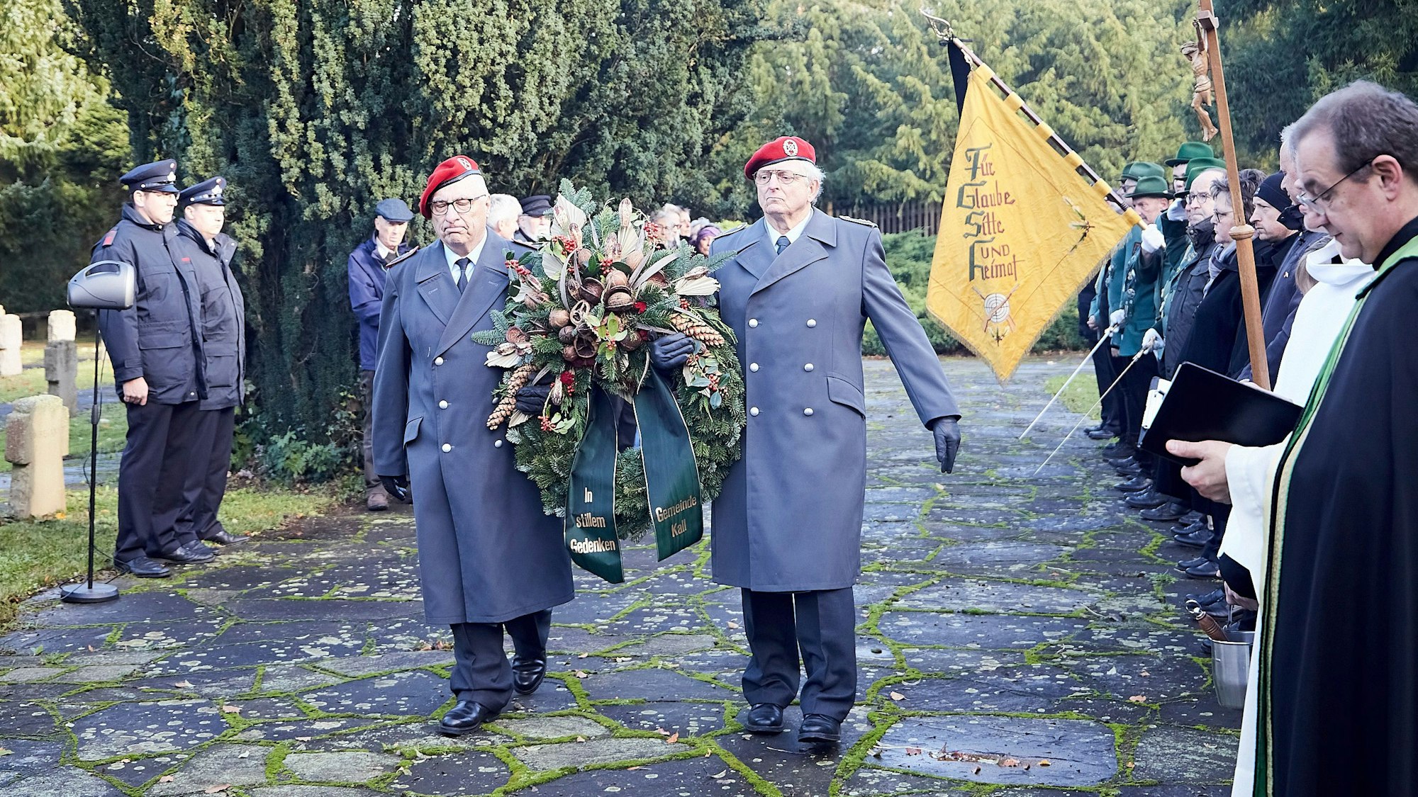 Zwei uniformierte Mitglieder der Reservistenkameradschaft tragen einen Kranz durch das Spalier der Teilnehmer.