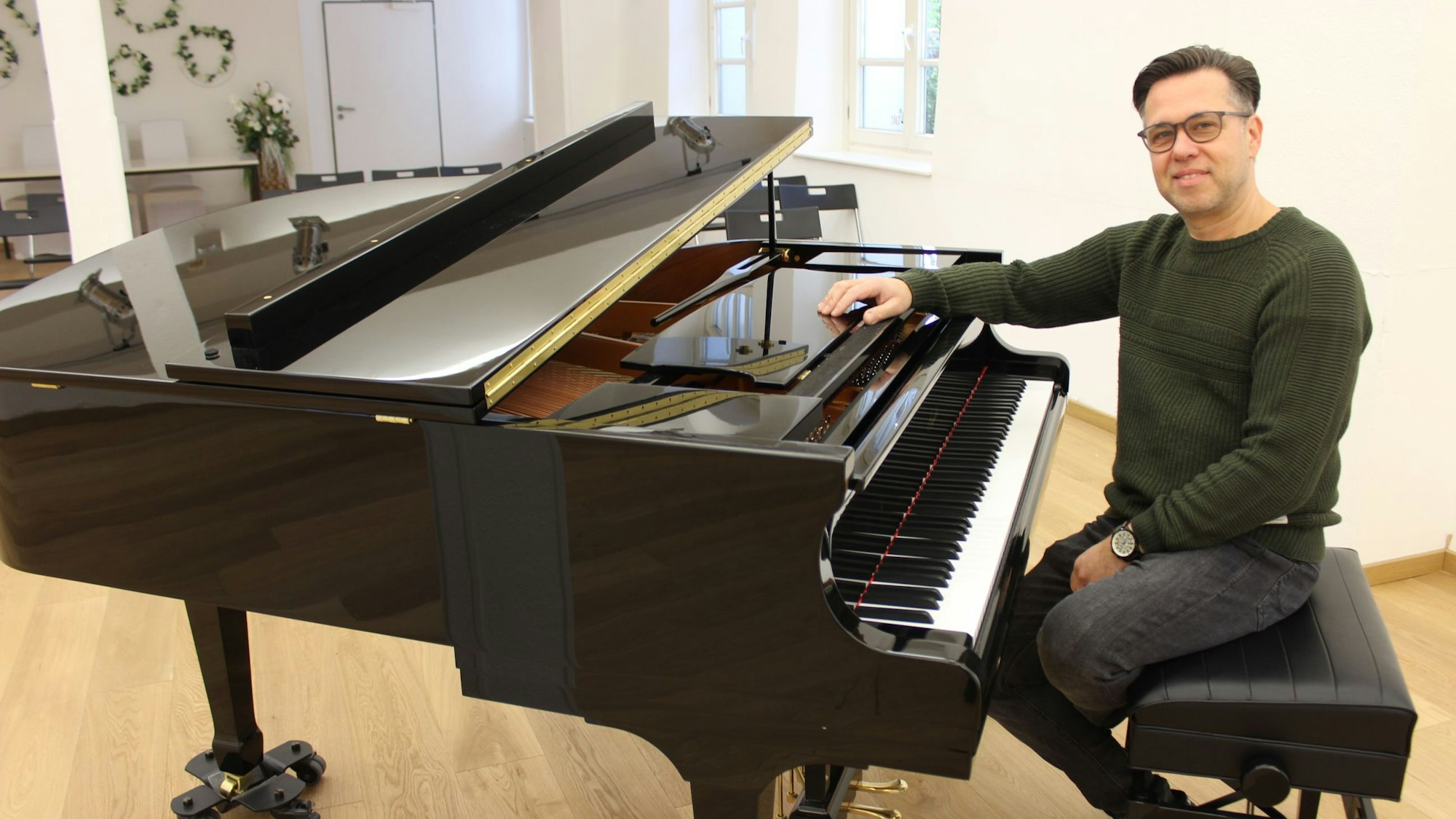 Ein Mann sitzt in einem Saal vor einem Flügel.