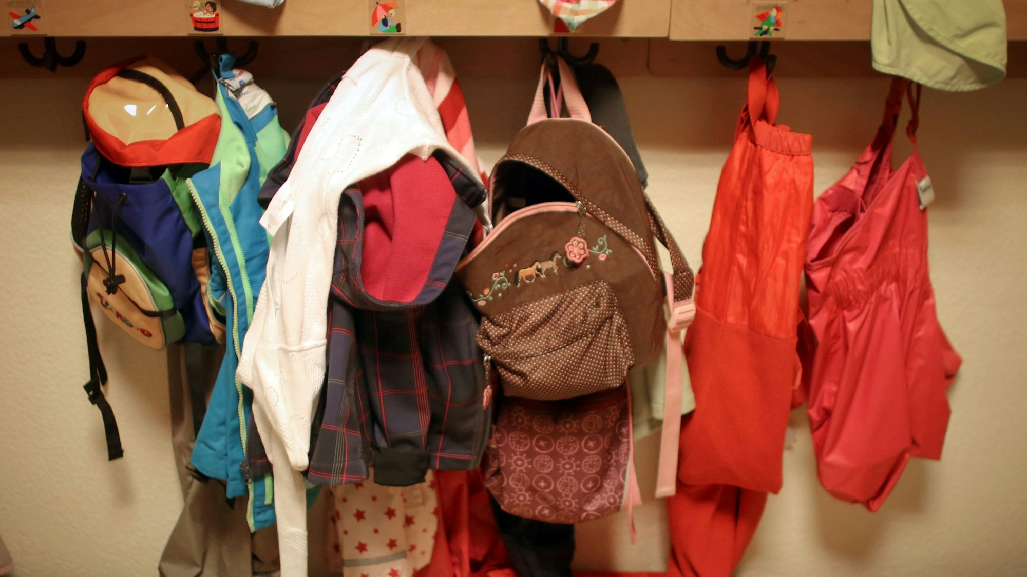Jacken und Rucksäcke von Kindern hängen in einer Kita.