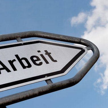 Ein Straßenschild beschriftet mit dem Wort „Arbeit“ vor blauem Himmel und Wolken.