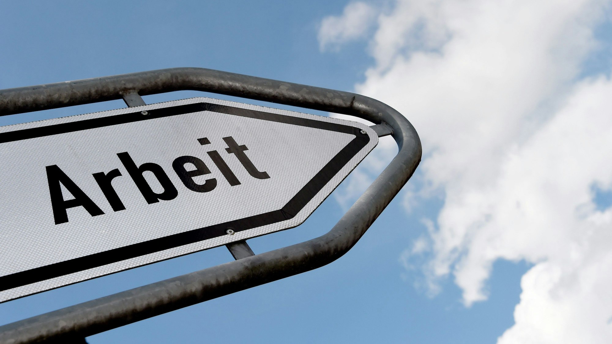 Ein Straßenschild beschriftet mit dem Wort „Arbeit“ vor blauem Himmel und Wolken.