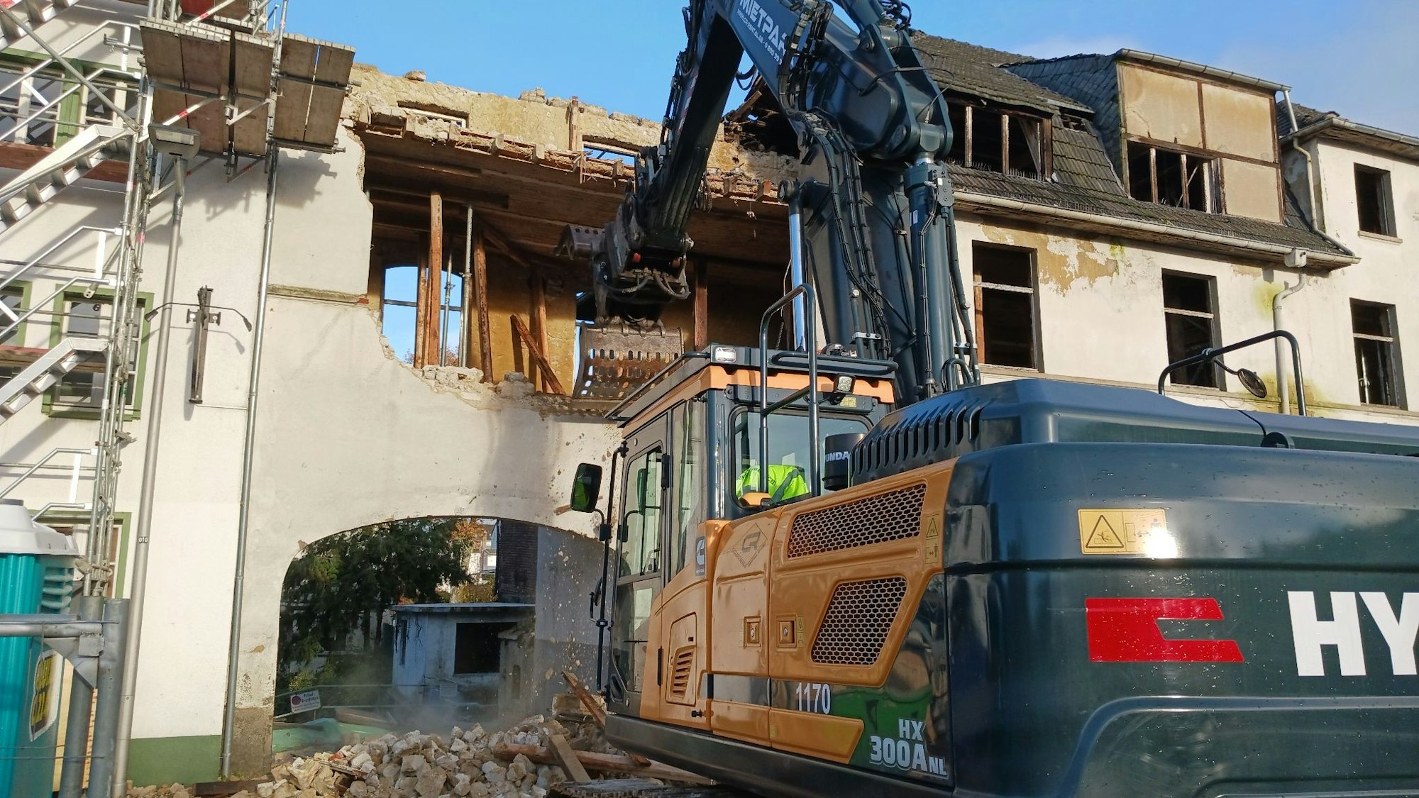 Ein Bagger reißt ein altes Haus ab, im ersten Stock klafft ein großes Loch