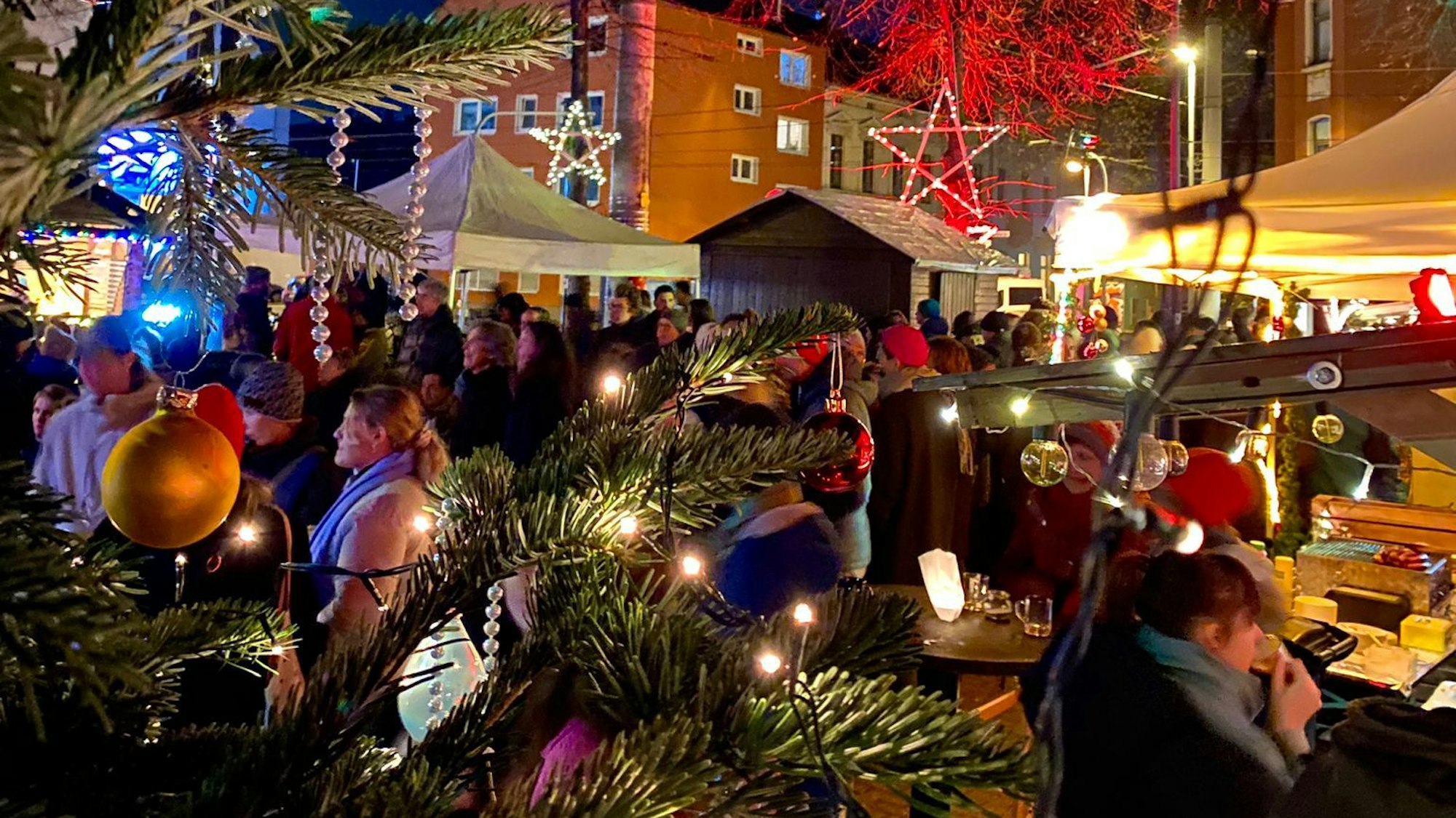 Auf einer Bühne im Freien stehen drei Musiker, vor der Bühne stehen viele Menschen mit Mützen.