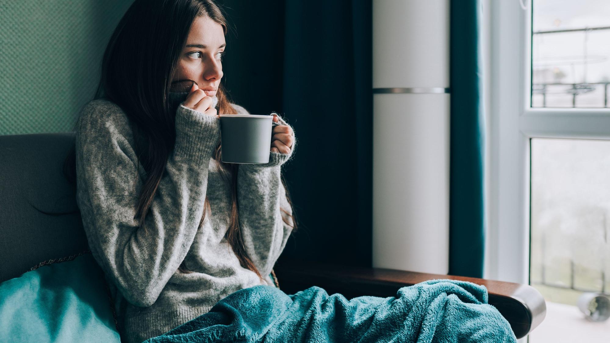 Frau friert auf dem Sofa mit Tasse Tee in der Hand