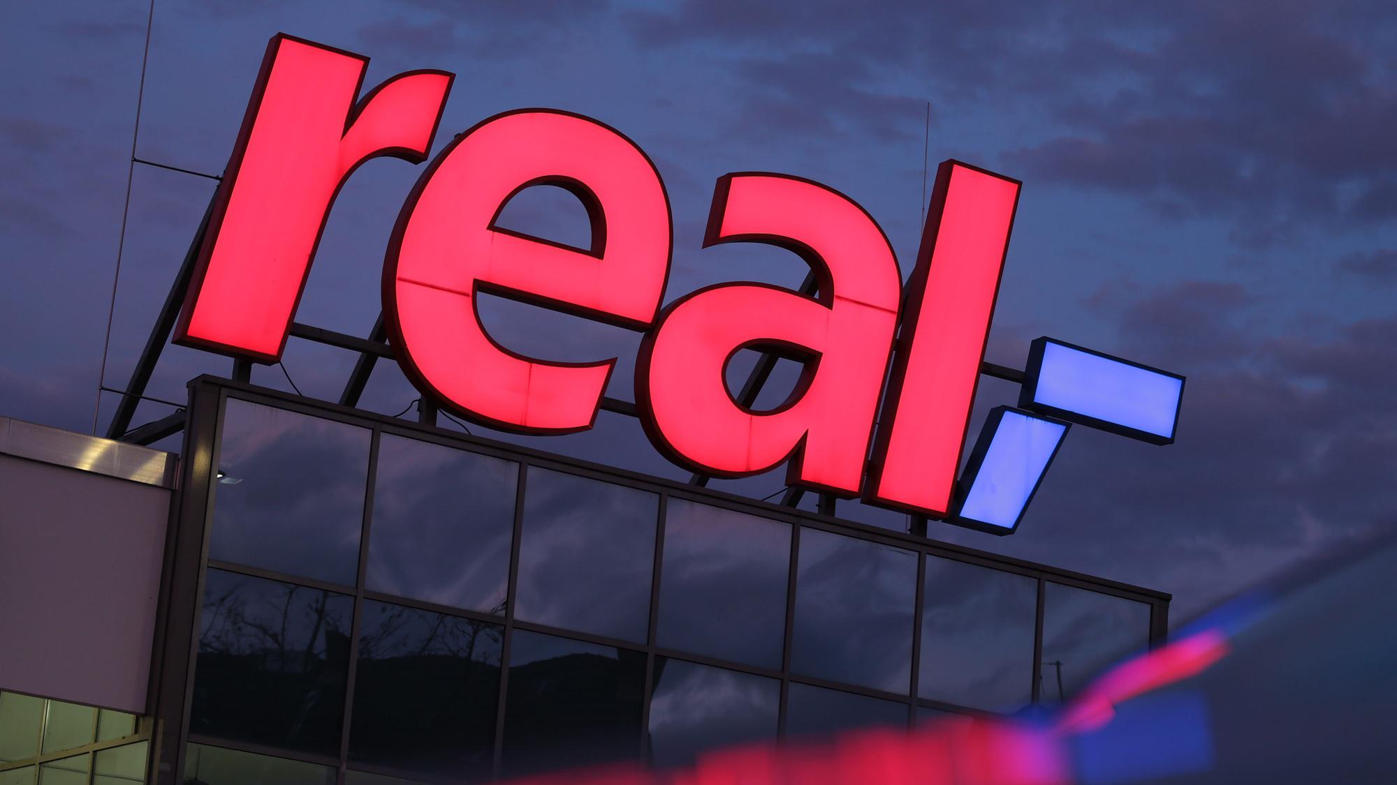 Das Logo leuchtet am Morgen auf dem Dach eines Real Supermarktes.