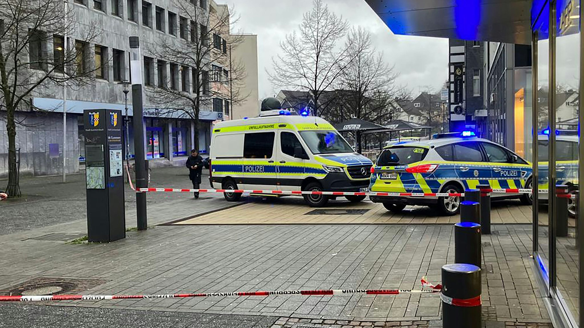 Zwei Polizeiwagen stehen in der Gummersbacher Innenstadt. Um ein Geschäft ist eine Fläche mit Flatterband abgesperrt.