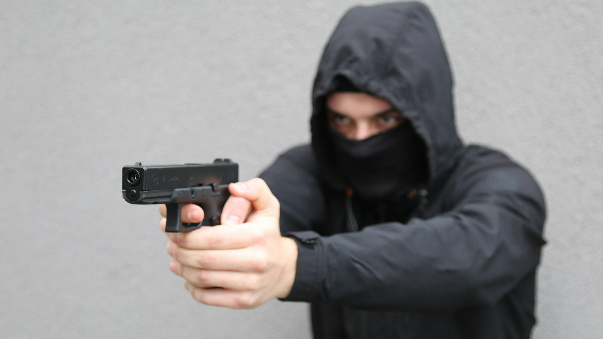 In einer gestellten Szene droht ein maskierter Mann mit einer Schusswaffe.