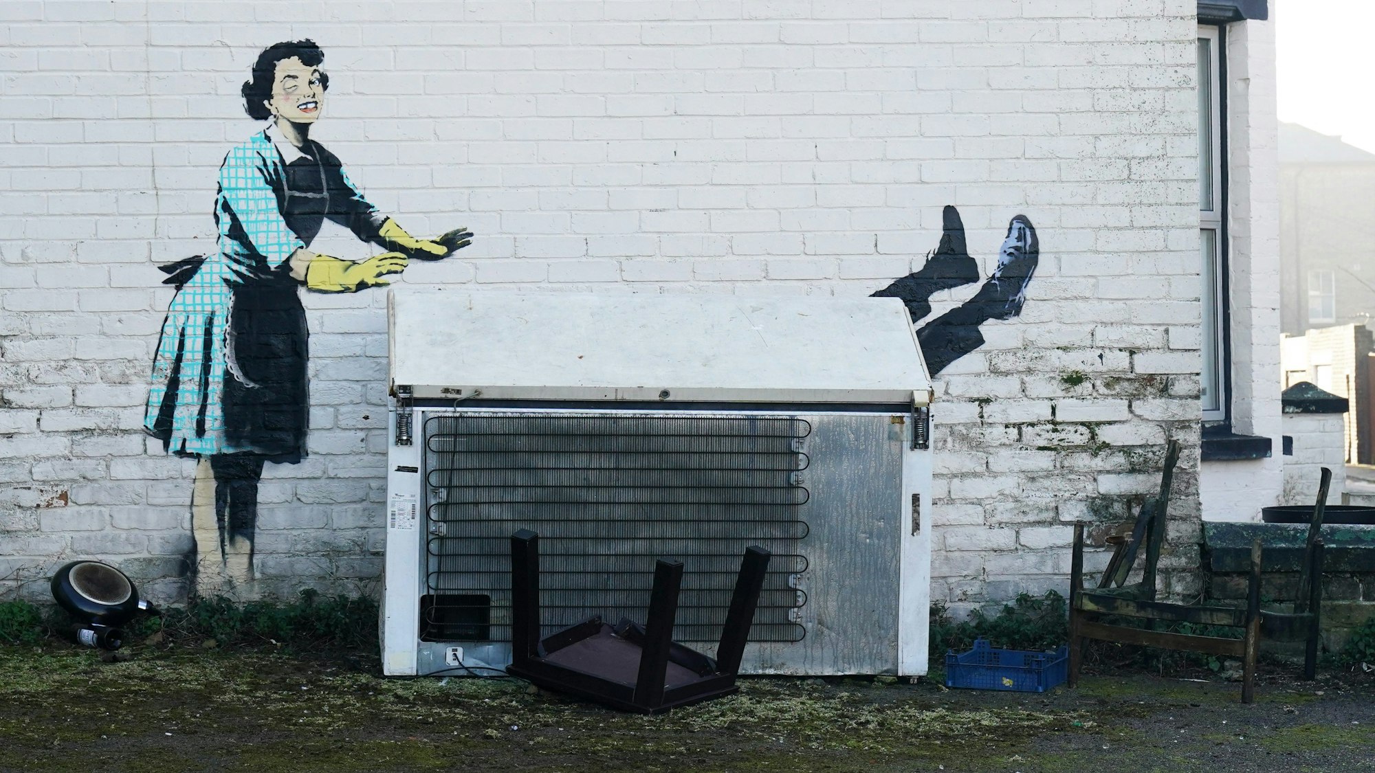 Blick auf das Kunstwerks „Valentine's Day Mascara“ des Künstlers Banksy an der Seite eines Gebäudes. Das Kunstwerk zeigt eine Hausfrau aus den 1950er Jahren, die eine klassische blaue Schürze und gelbe Spülhandschuhe trägt, ein geschwollenes Auge und einen fehlenden Zahn hat und ihren Partner scheinbar in eine Gefriertruhe schiebt.