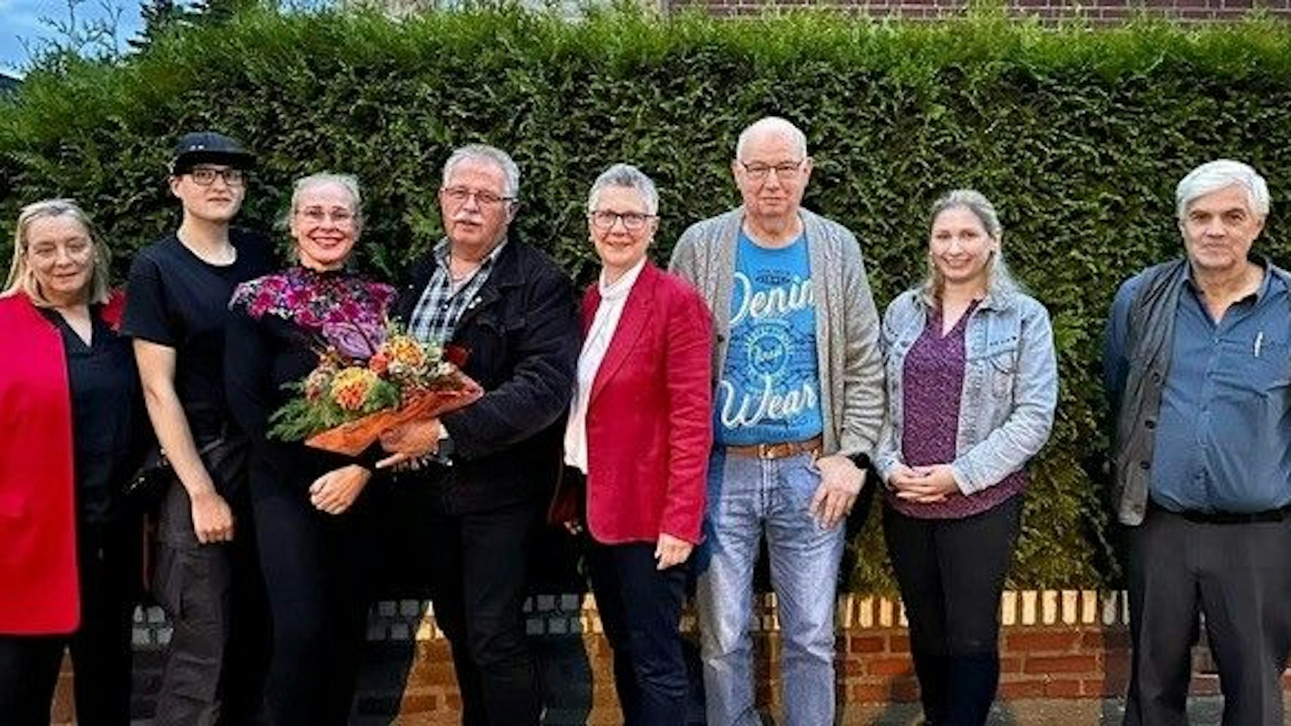 Männer und Frauen stehen nebeneinander. Einer hält einen Blumenstrauß.