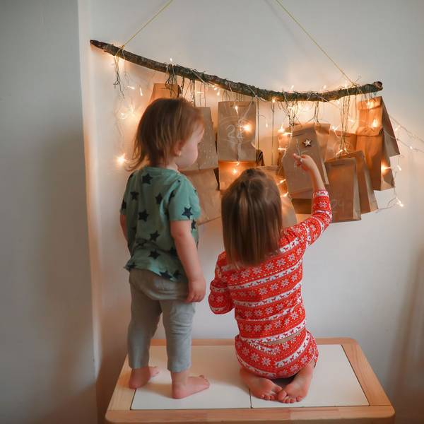 Zwei kleine Kinder stehen vor einem erleuchteten Adventskalender.