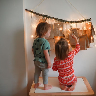 Zwei kleine Kinder stehen vor einem erleuchteten Adventskalender.