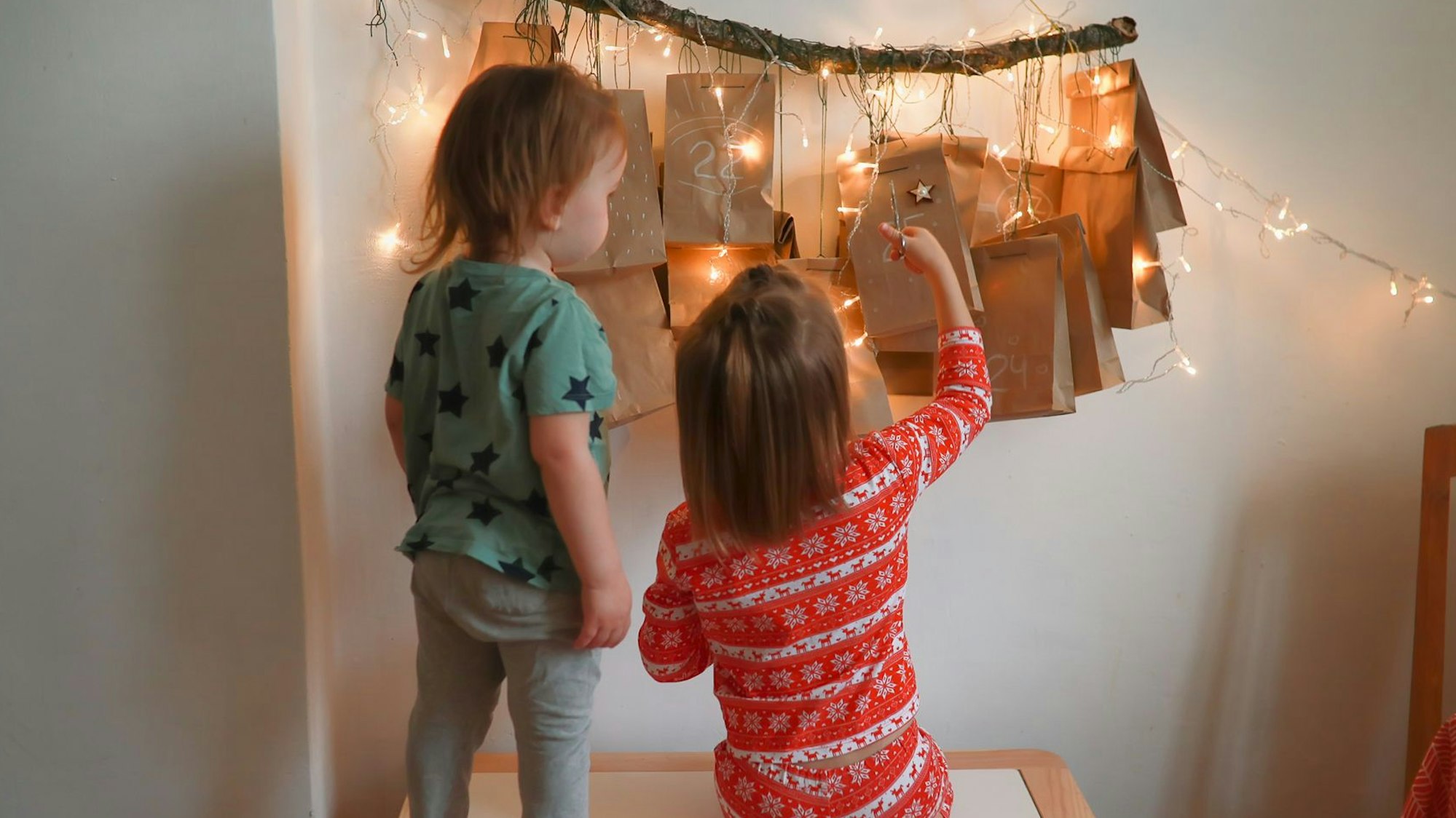 Zwei kleine Kinder stehen vor einem erleuchteten Adventskalender.