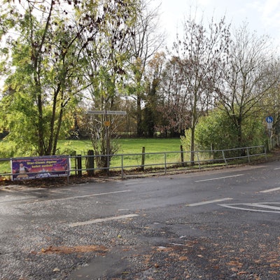 Die Einmündung auf eine von Wiesen gesäumte Straße ist zu sehen.