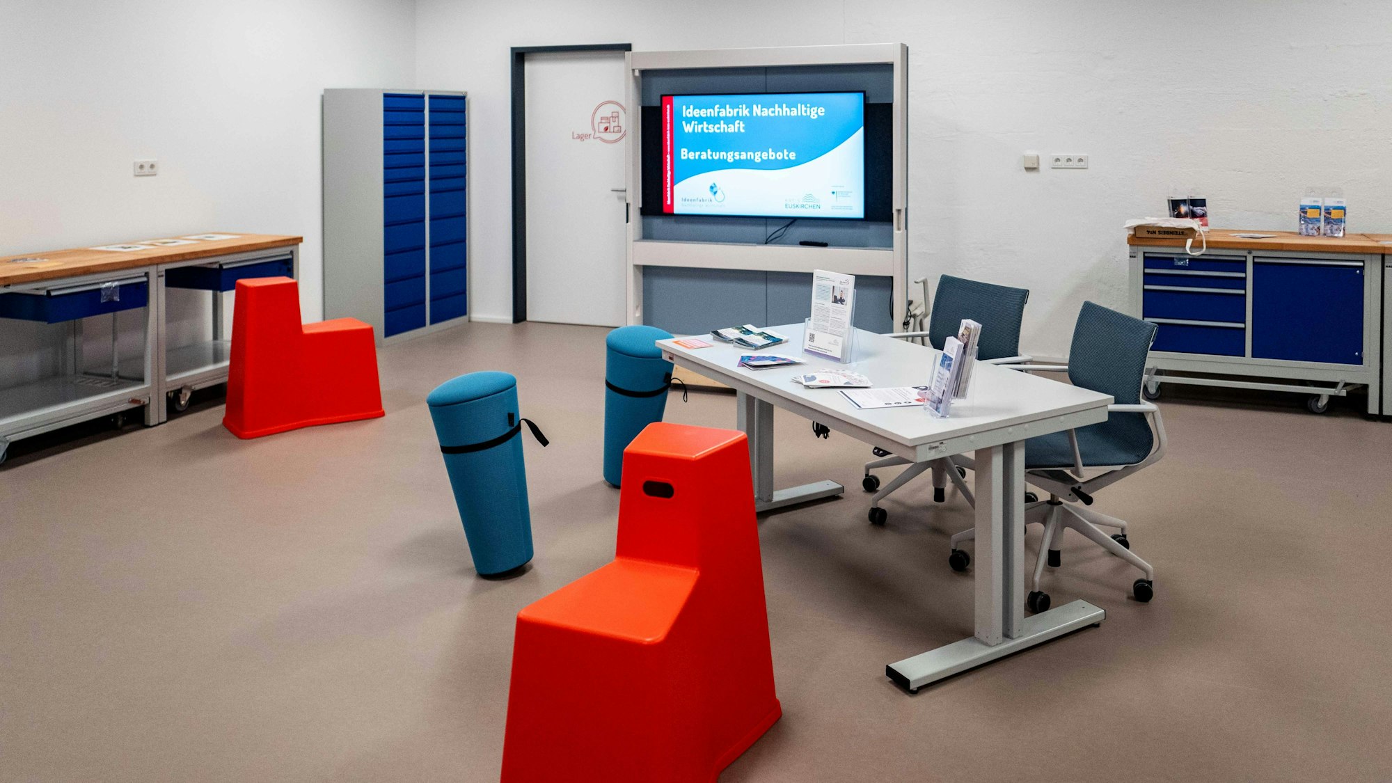 Das Bild zeigt eine moderne Werkstatt mit roten und blauen Sitzgelegenheiten und einem Schreibtisch.