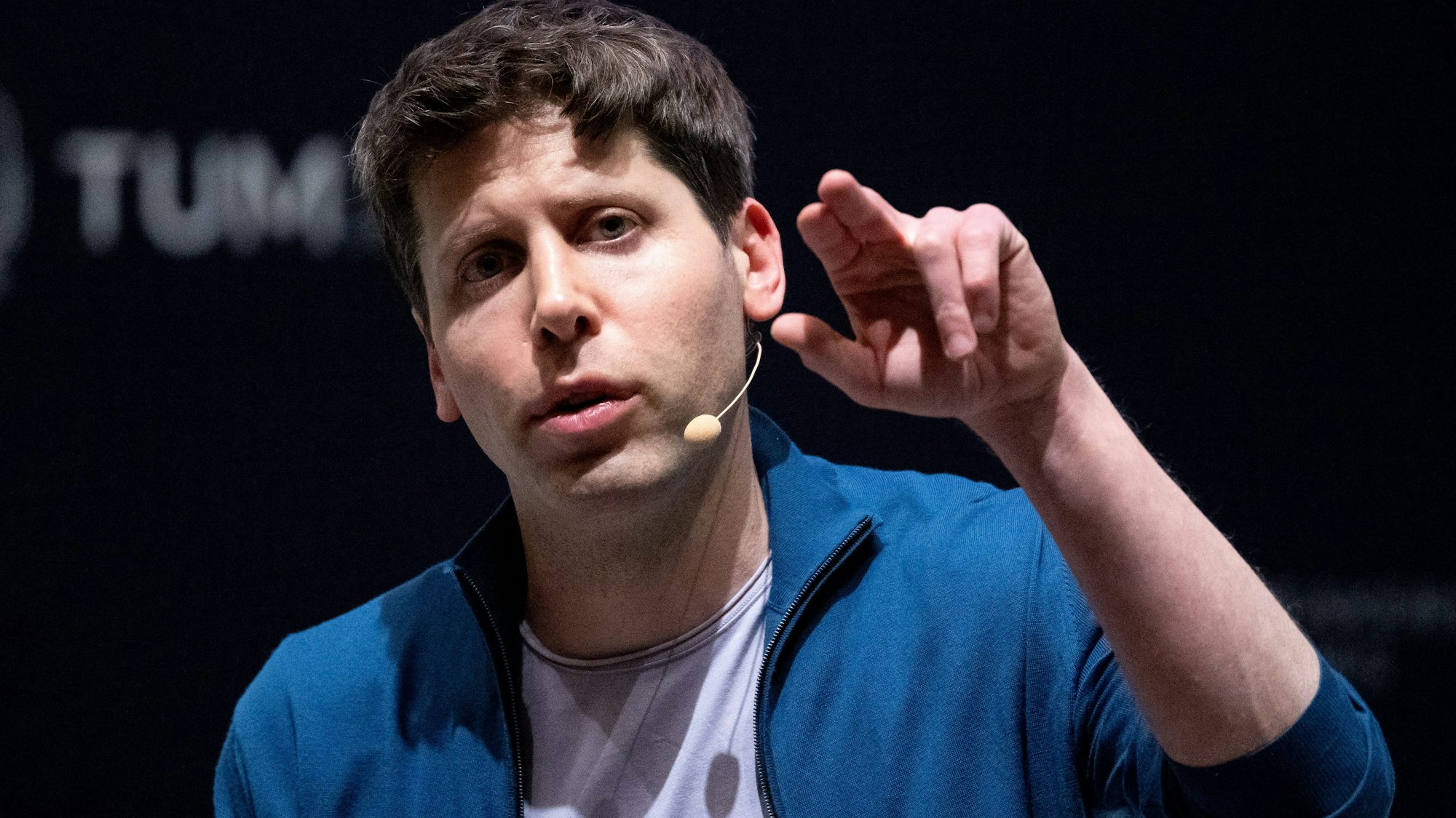Bayern, München: Sam Altman, Geschäftsführer (CEO) von OpenAI und Erfinder der KI-Software ChatGPT, nimmt an der Technische Universität München (TUM) an einer Podiumsdiskussion teil. Er trägt eine blaue Jacke zum T-Shirt und gestikuliert mit zwei ausgestreckten Fingern.