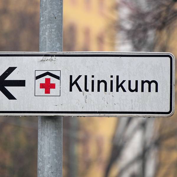 Ein Schild mit rotem Kreuz weist den Weg zu einem Klinikum.
