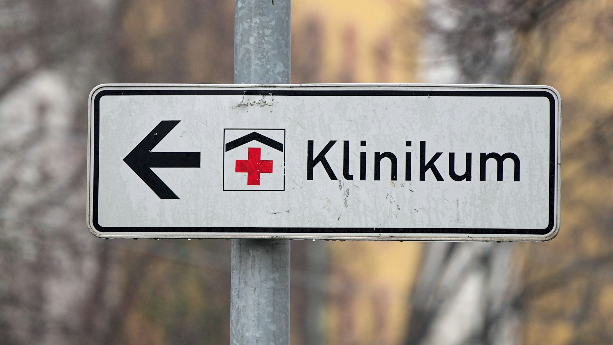 Ein Schild mit rotem Kreuz weist den Weg zu einem Klinikum.