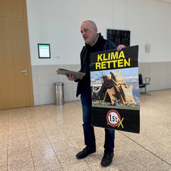 Klima-Aktivist Winfried Bernhard in Düsseldorf vor Gericht. Auf seinem Protestplakat: Das umstrittene Foto, das ihn vor einem Tagebaubagger zeigt. Er steht vor Gericht, weil er ein im Landtag ausgestelltes Bild mit Kartoffelbrei beschmiert hatte. Das als Pressefoto des Jahres ausgezeichnete Bild zeigt ihn selbst, wie er vor einem Braunkohlebagger im Rheinischen Revier kniet.