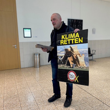 Klima-Aktivist Winfried Bernhard in Düsseldorf vor Gericht. Auf seinem Protestplakat: Das umstrittene Foto, das ihn vor einem Tagebaubagger zeigt. Er steht vor Gericht, weil er ein im Landtag ausgestelltes Bild mit Kartoffelbrei beschmiert hatte. Das als Pressefoto des Jahres ausgezeichnete Bild zeigt ihn selbst, wie er vor einem Braunkohlebagger im Rheinischen Revier kniet.