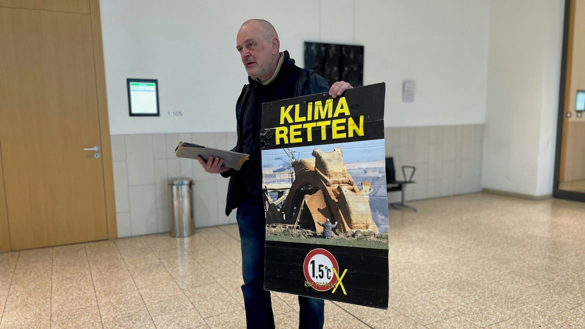 Klima-Aktivist Winfried Bernhard in Düsseldorf vor Gericht. Auf seinem Protestplakat: Das umstrittene Foto, das ihn vor einem Tagebaubagger zeigt. Er steht vor Gericht, weil er ein im Landtag ausgestelltes Bild mit Kartoffelbrei beschmiert hatte. Das als Pressefoto des Jahres ausgezeichnete Bild zeigt ihn selbst, wie er vor einem Braunkohlebagger im Rheinischen Revier kniet.