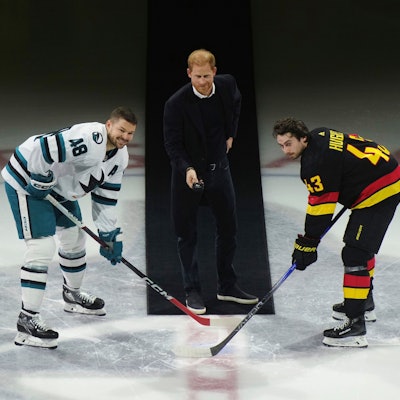 Prinz Harry (Mitte) wirft den Puck zu Tomas Hertl (links) von den San Jose Sharks und Quinn Hughes (rechts) von den Vancouver Canucks während eines feierlichen Eröffnungsspiels vor einem NHL-Eishockeyspiel in Vancouver, British Columbia.