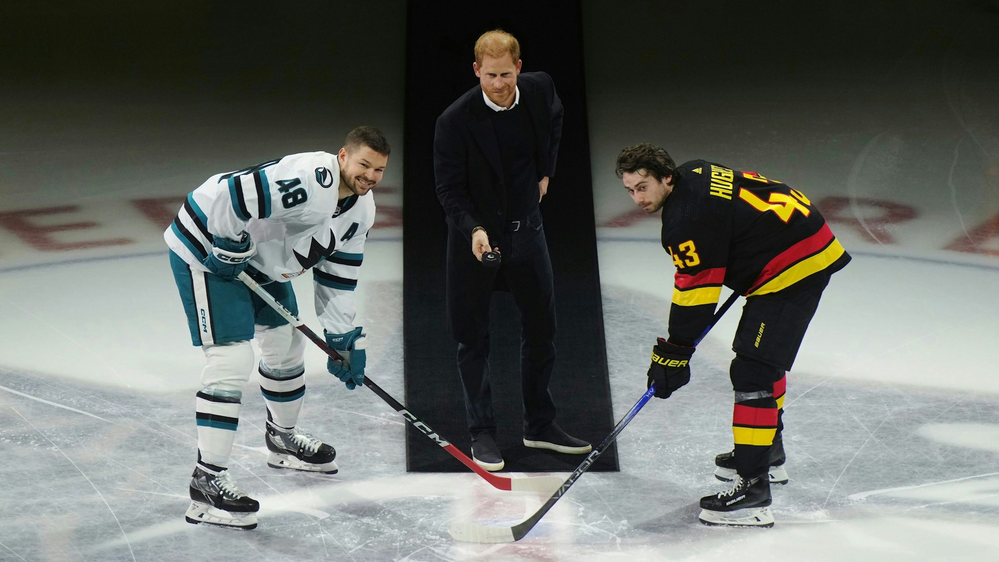 Prinz Harry (Mitte) wirft den Puck zu Tomas Hertl (links) von den San Jose Sharks und Quinn Hughes (rechts) von den Vancouver Canucks während eines feierlichen Eröffnungsspiels vor einem NHL-Eishockeyspiel in Vancouver, British Columbia.