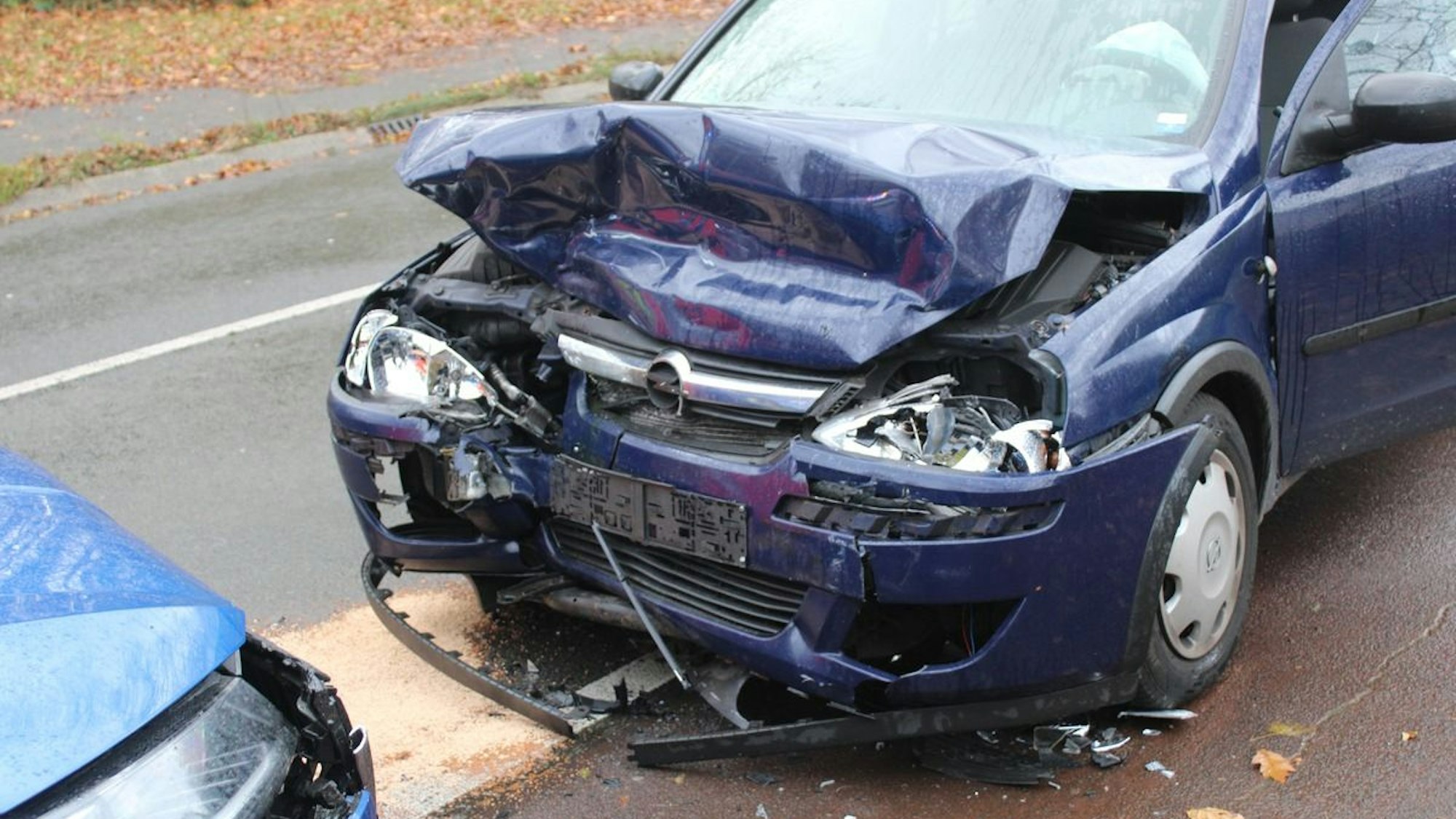 Ein beschädigter Pkw steht an einer Unfallstelle auf einer Straße.