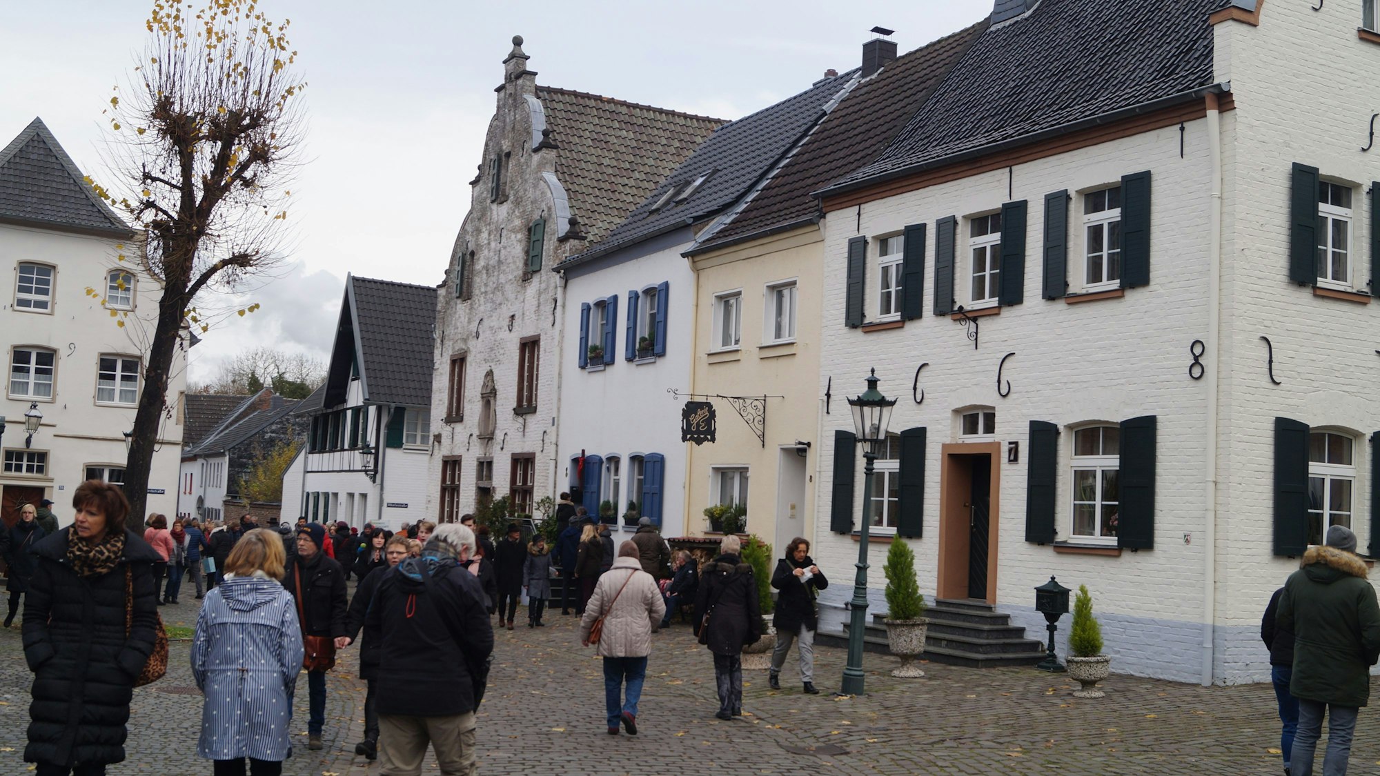 Viele Menschen in Winterkleidung gehen über ein Kopfsteinpflaster zwischen alten Häusern umher.