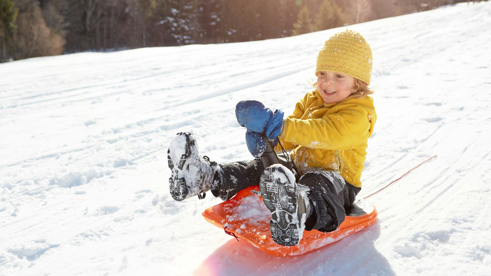 Ein kleines Kind sitzt auf einem orangenen Schlitten.