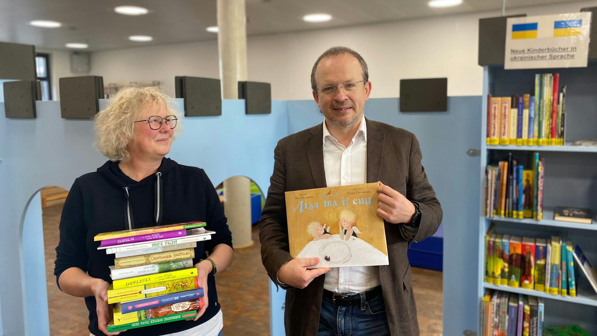 Zwei Personen stehen in der Kinderabteilung einer Bibliothek und halten Bücher.