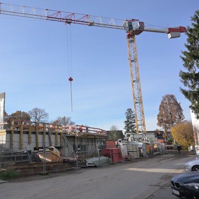 Der Rohbau des Erdgeschosses des neuen Schulgebäudes sowie Arbeitsmaterialien und ein gelber Baukran sind zu sehen.