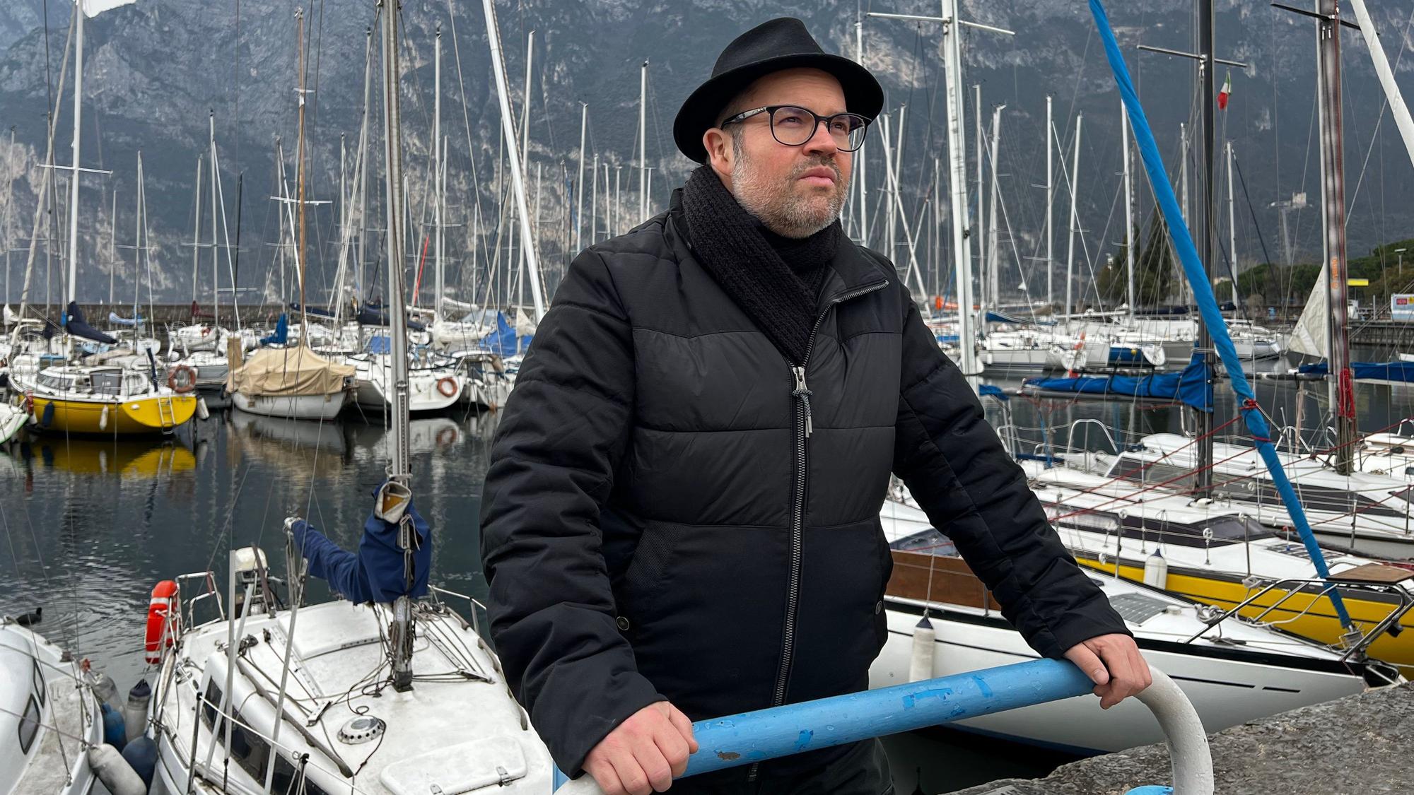 Björn Heuser steht am Gardasee an einem Hafen.