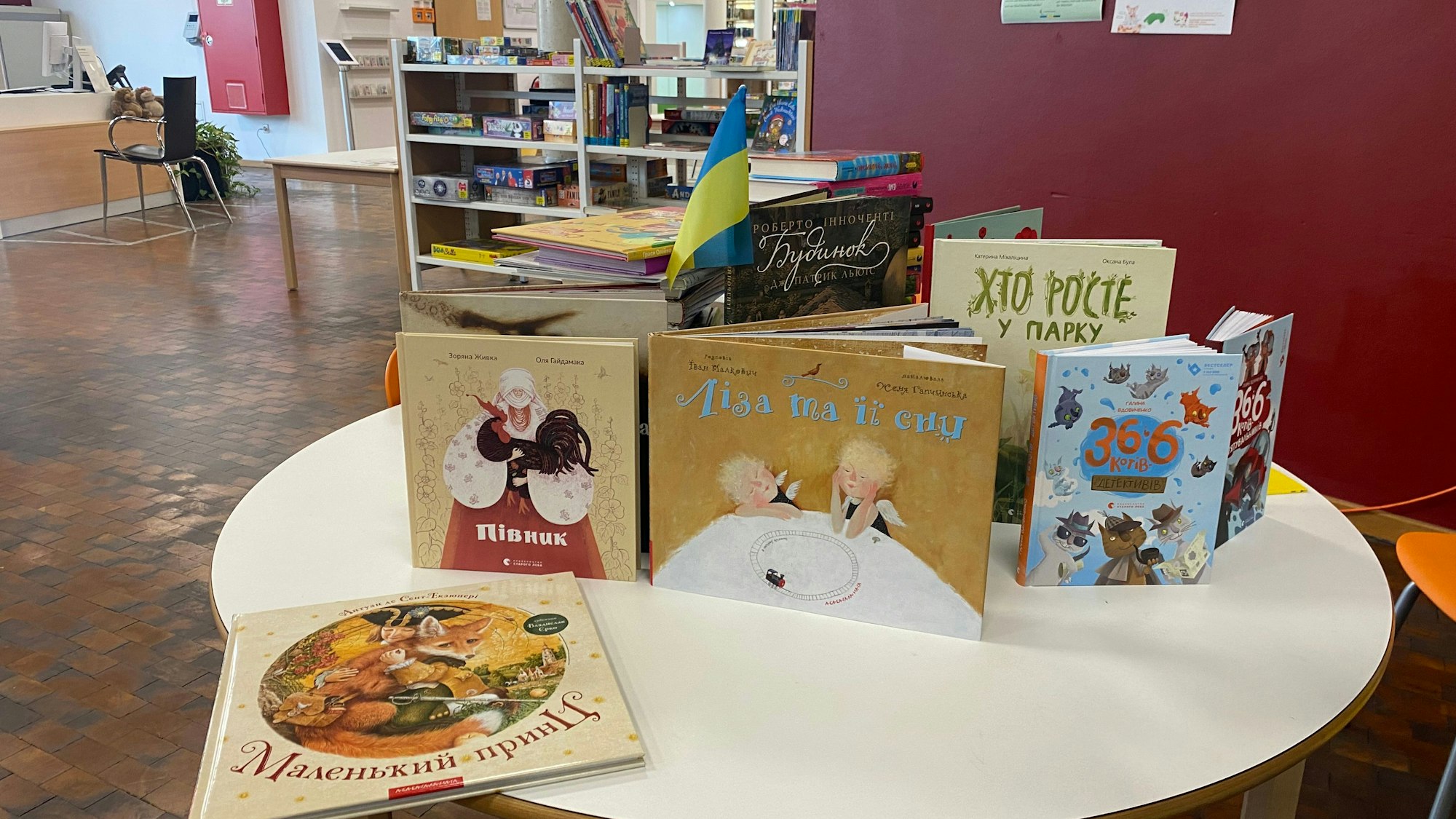 Auf einem Tisch in einer Bibliothek stehen Bücher aufgestellt. In einem steckt eine Ukraine-Flagge.
