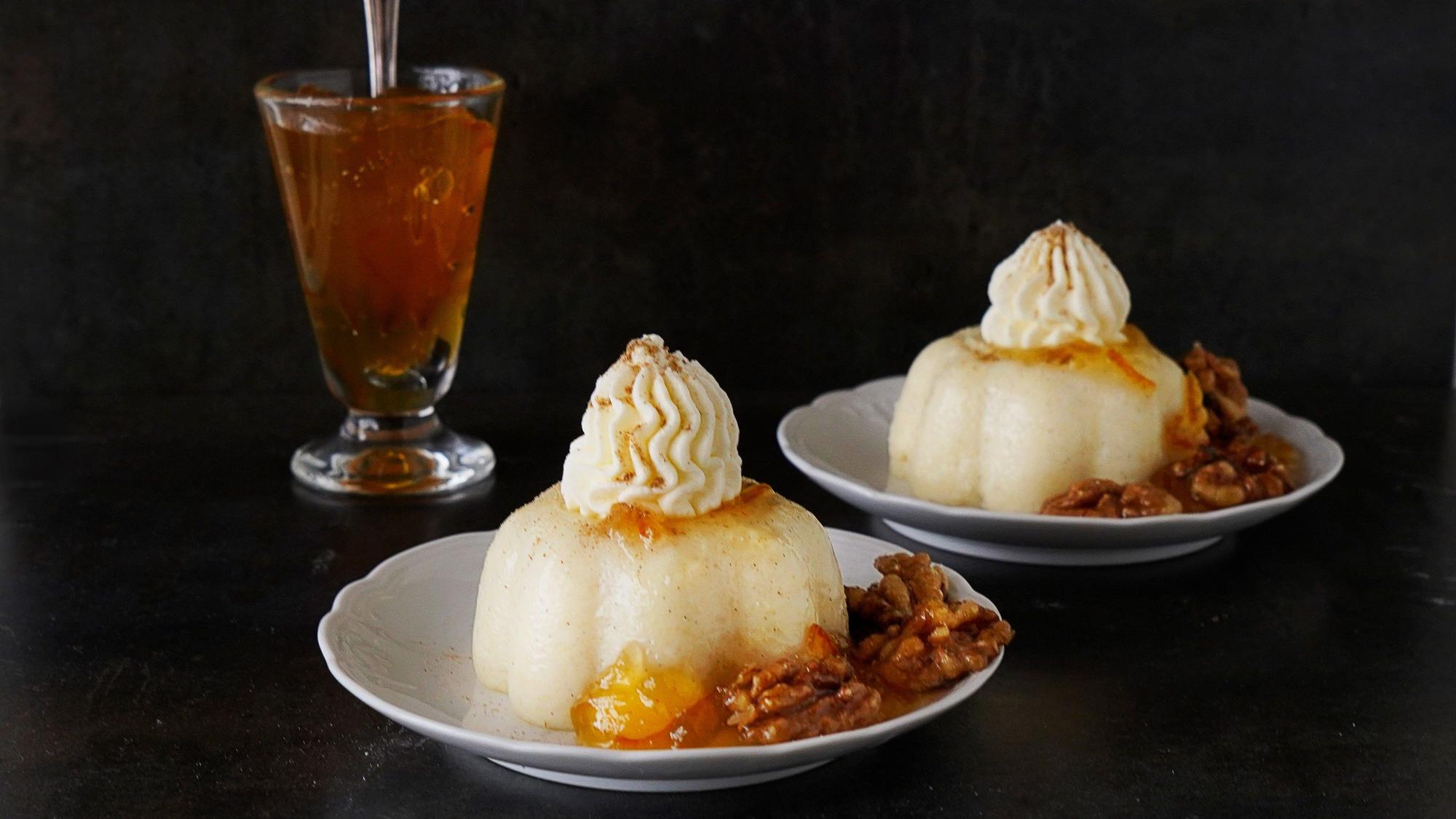 Auf zwei Teller ist je ein Pudding mit Sahnehaube angerichtet. Neben dem Pudding liegen mehrere Walnüsse.