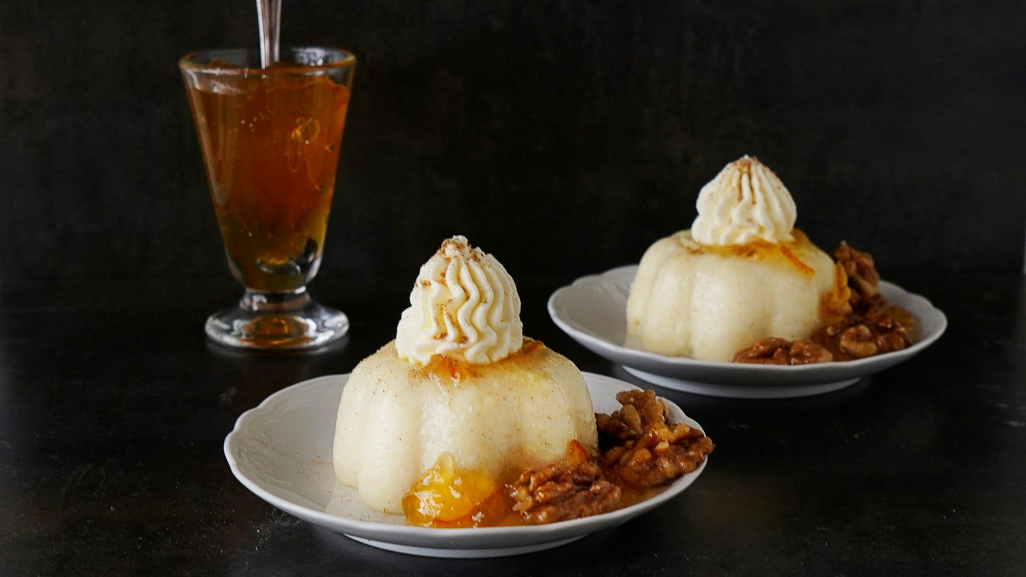 Auf zwei Teller ist je ein Pudding mit Sahnehaube angerichtet. Neben dem Pudding liegen mehrere Walnüsse.